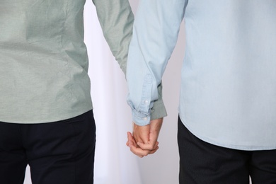 Gay couple holding hands on light background, closeup view