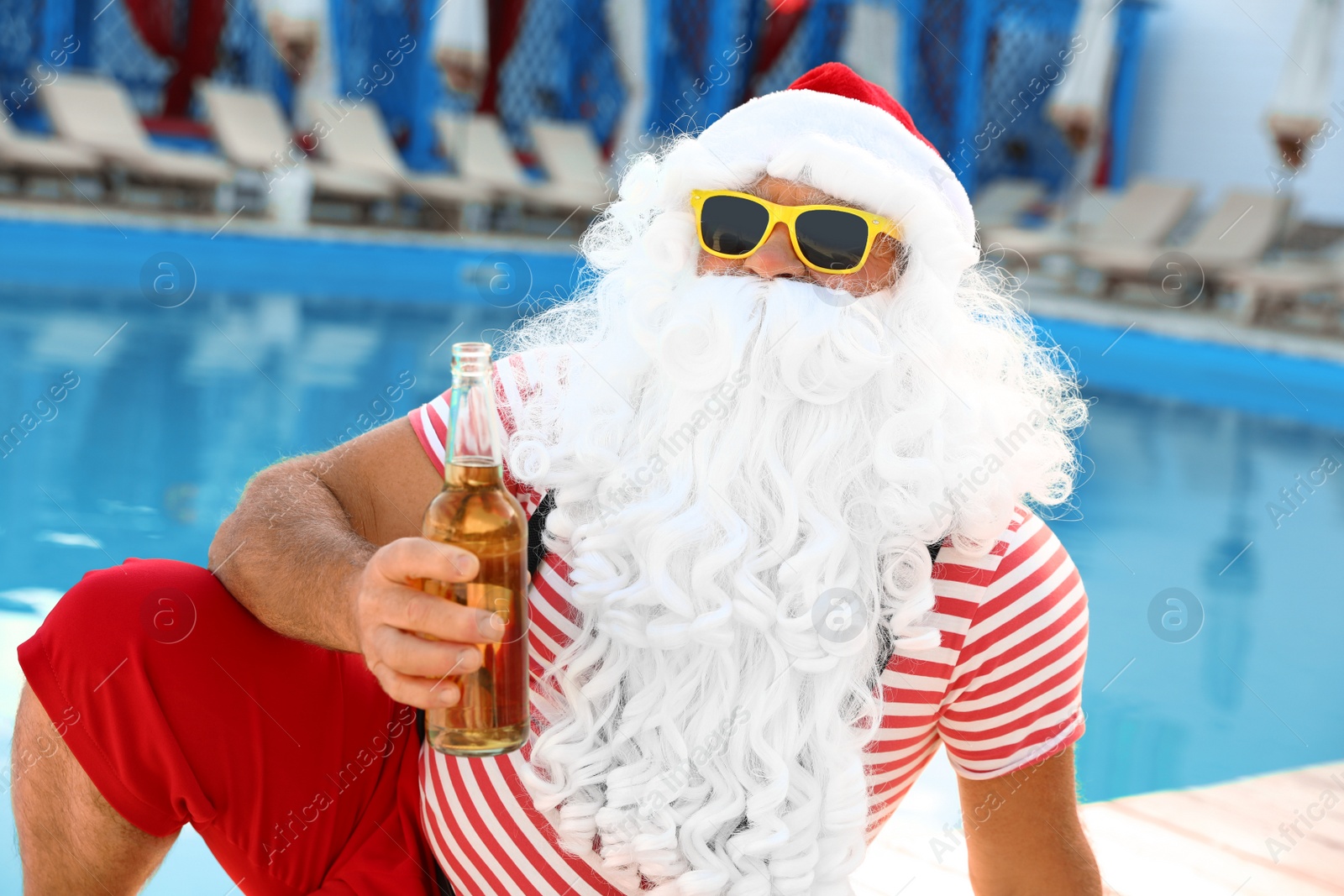 Photo of Authentic Santa Claus with bottle of beer near pool at resort