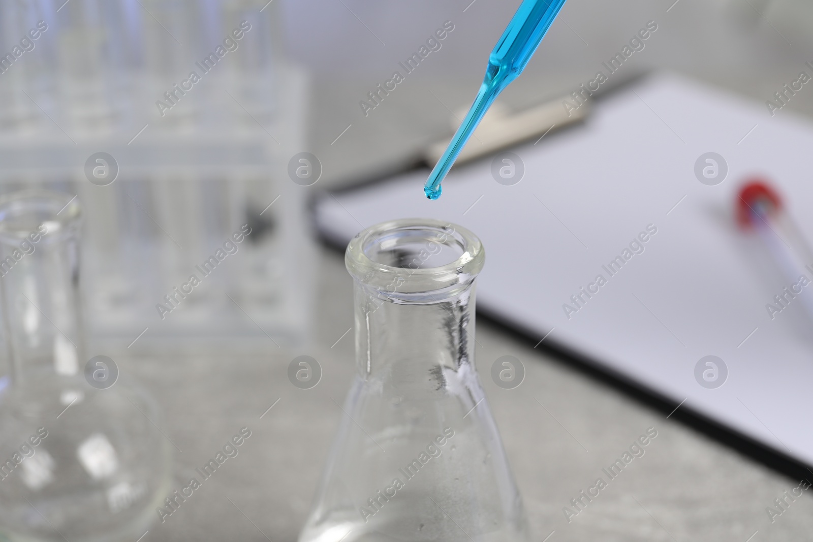 Photo of Laboratory analysis. Dripping liquid into flask on light grey table, closeup