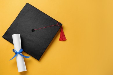 Photo of Graduation hat and diploma on yellow background, flat lay. Space for text
