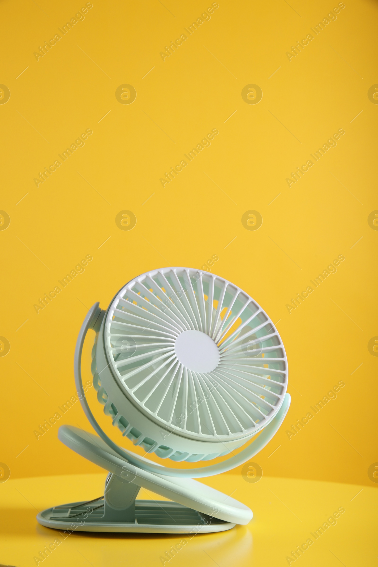 Photo of Modern electric fan on table against yellow background