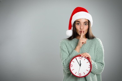 Photo of Woman in Santa hat with clock on grey background, space for text. New Year countdown