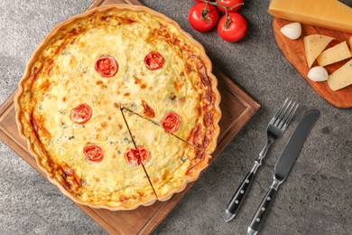 Photo of Delicious homemade cheese quiche, cutlery and ingredients on gray table, flat lay