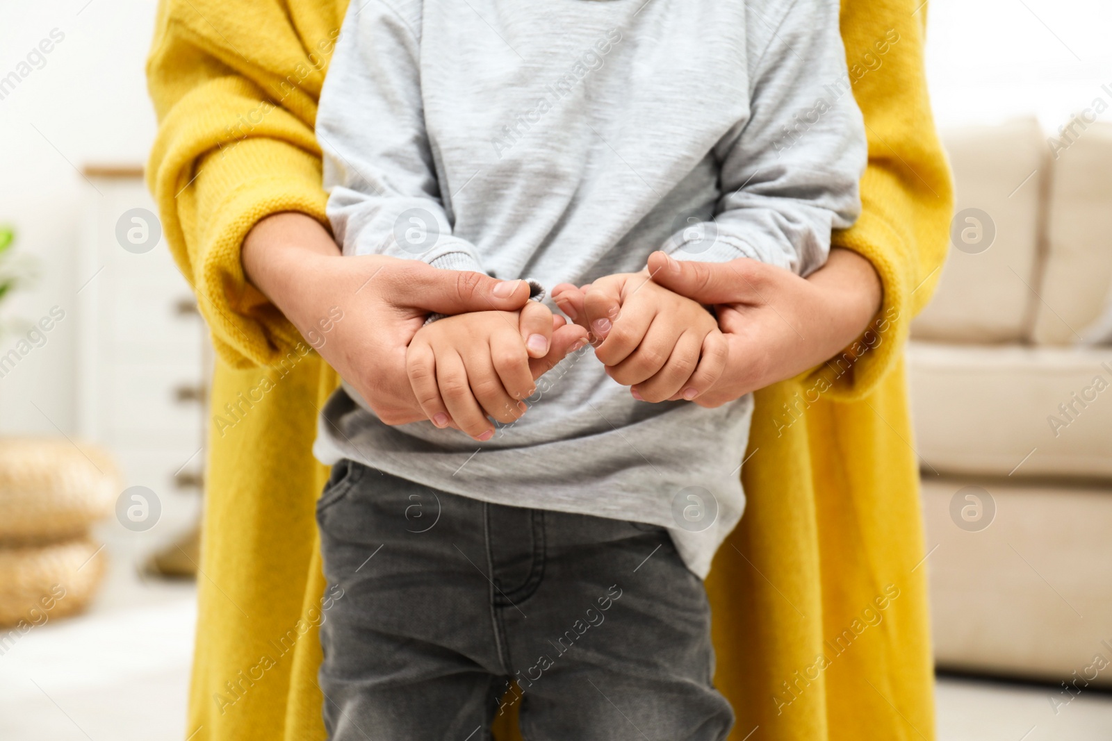 Photo of Mother holding hands with her child indoors, closeup. Happy family