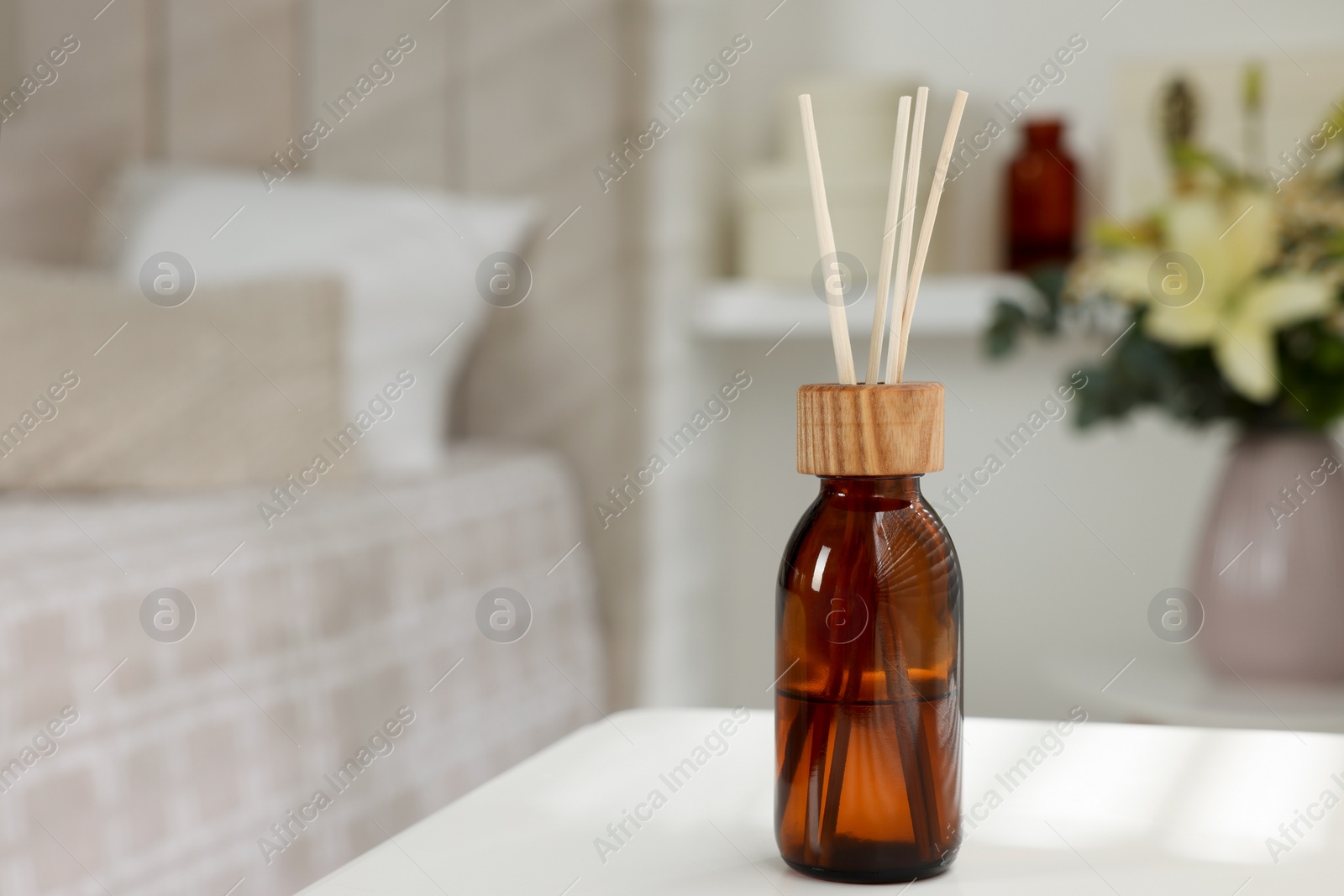 Photo of Aromatic reed air freshener on white table in bedroom. Space for text