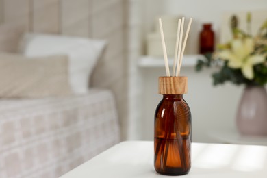 Photo of Aromatic reed air freshener on white table in bedroom. Space for text