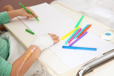 Photo of Little child with infusion drip drawing in hospital bed, closeup