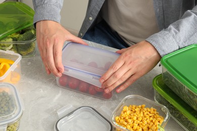 Man closing plastic container with lid at light grey marble table in kitchen, closeup. Food storage