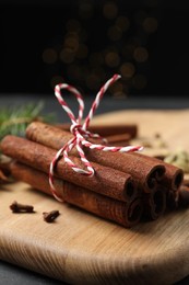 Cinnamon sticks and other spices on table against black background with blurred lights, closeup