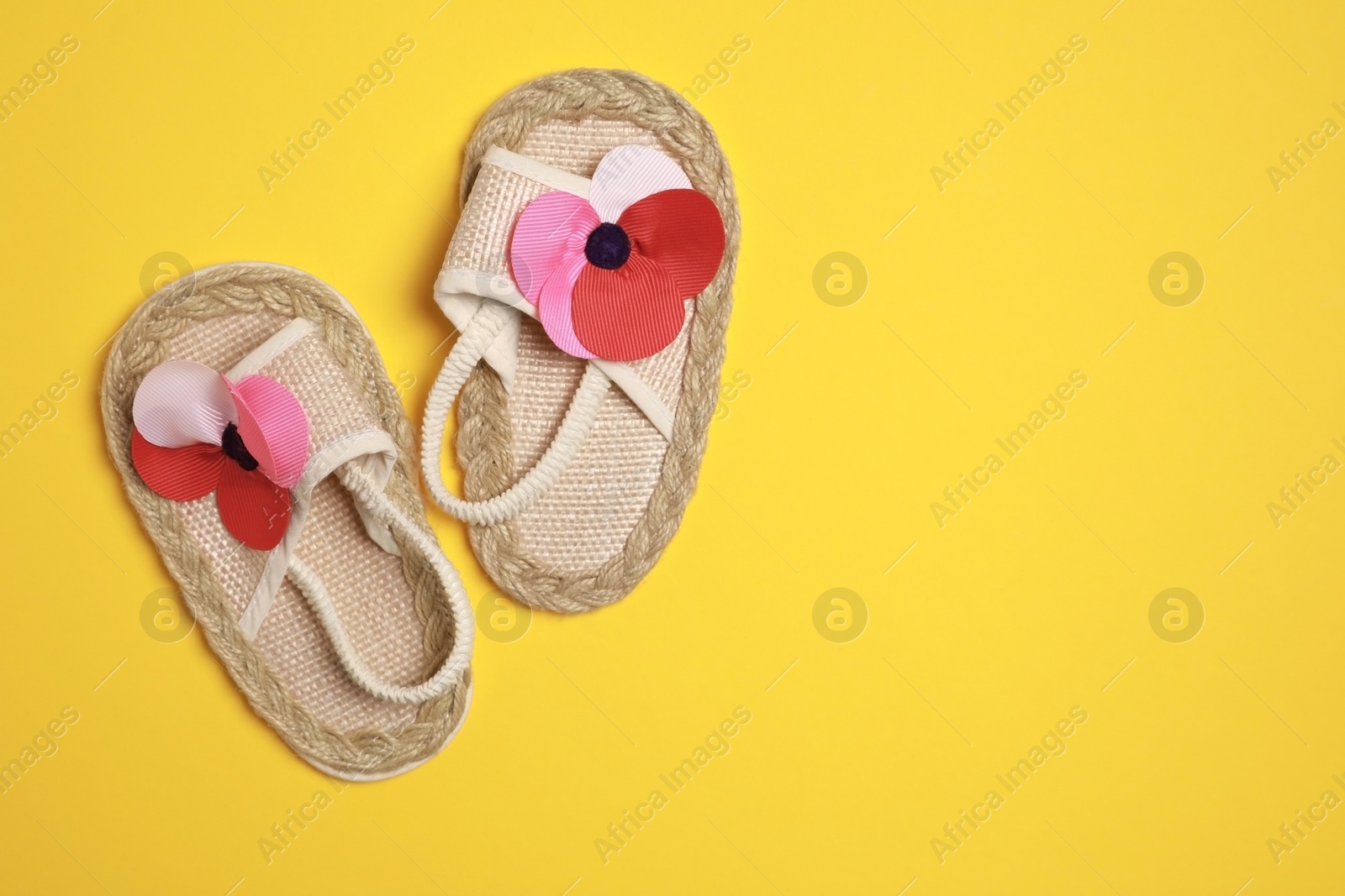 Photo of Cute baby shoes on yellow background, flat lay. Space for text