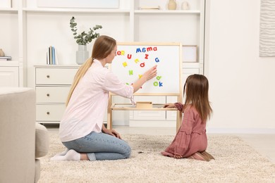 Photo of Mom teaching her daughter alphabet with magnetic letters at home