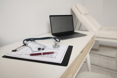 Photo of Clipboard, stethoscope, laptop and pen on white table in clinic. Doctor's workplace