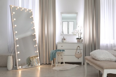 Large mirror with light bulbs and chest of drawers in bedroom. Interior design