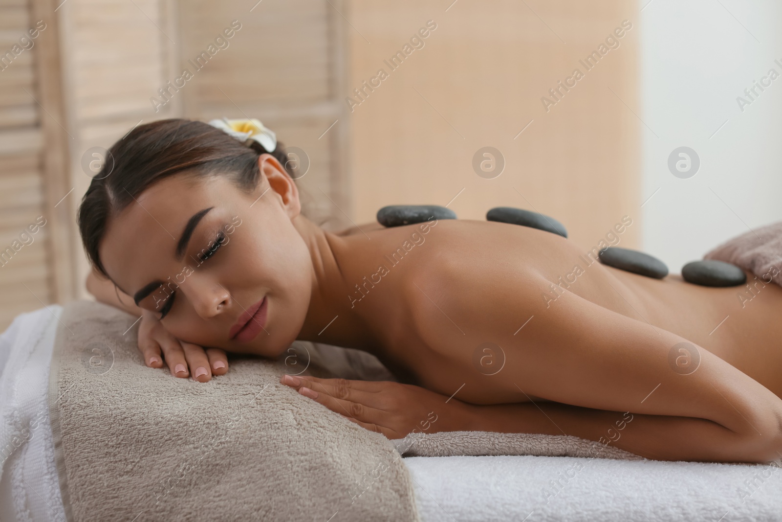 Photo of Beautiful young woman getting hot stone massage in spa salon