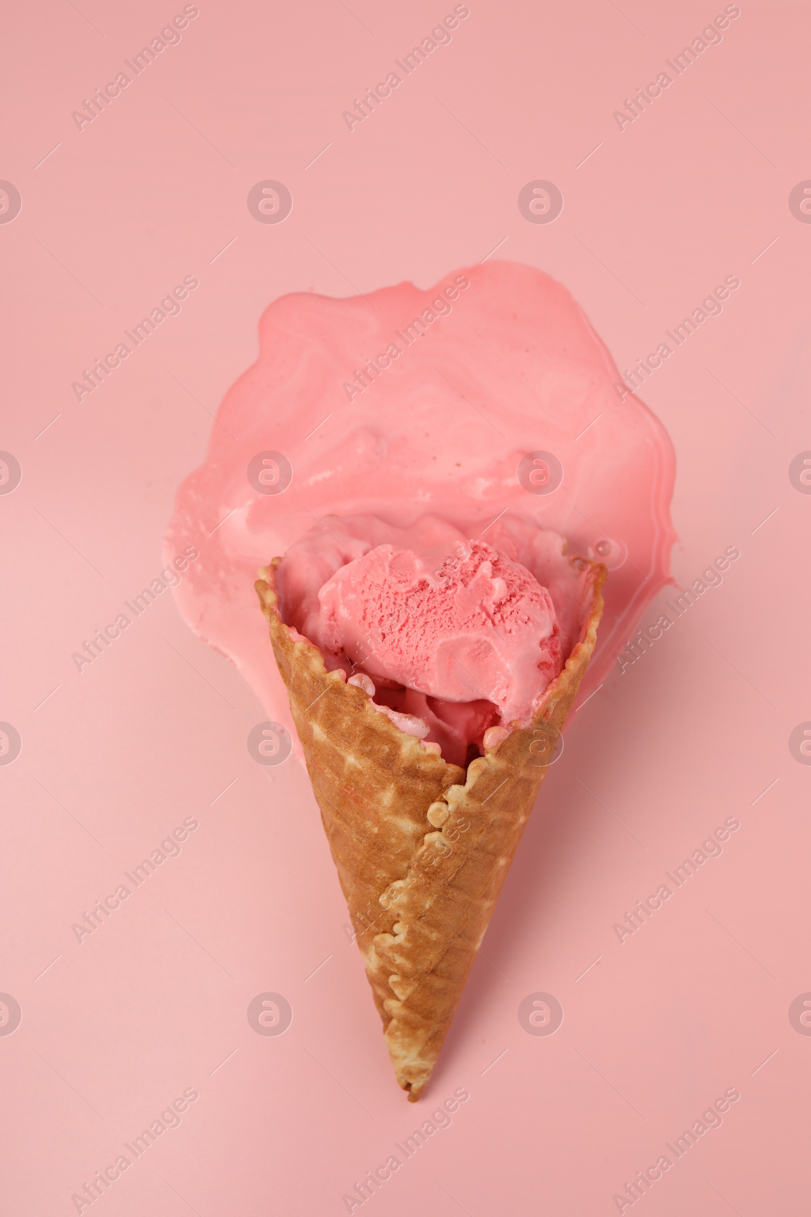 Photo of Melted ice cream in wafer cone on pink background, top view