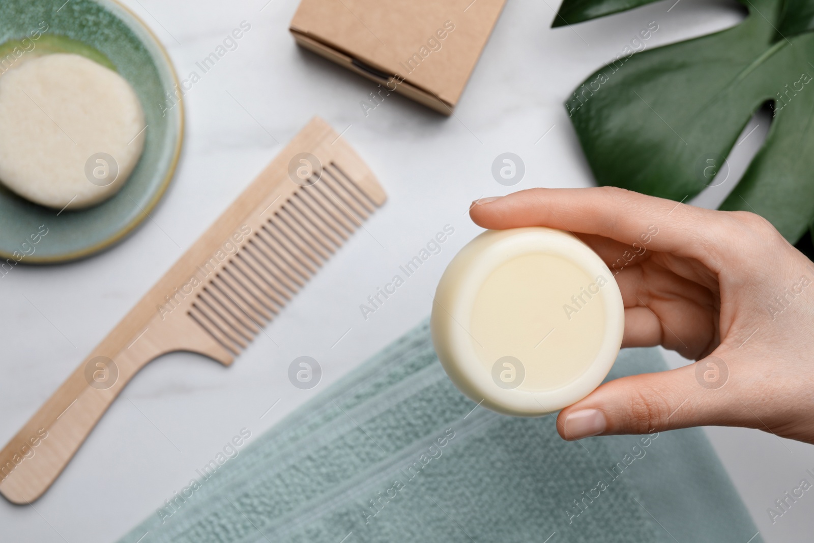 Photo of Woman holding solid shampoo bar at marble table, top view. Hair care