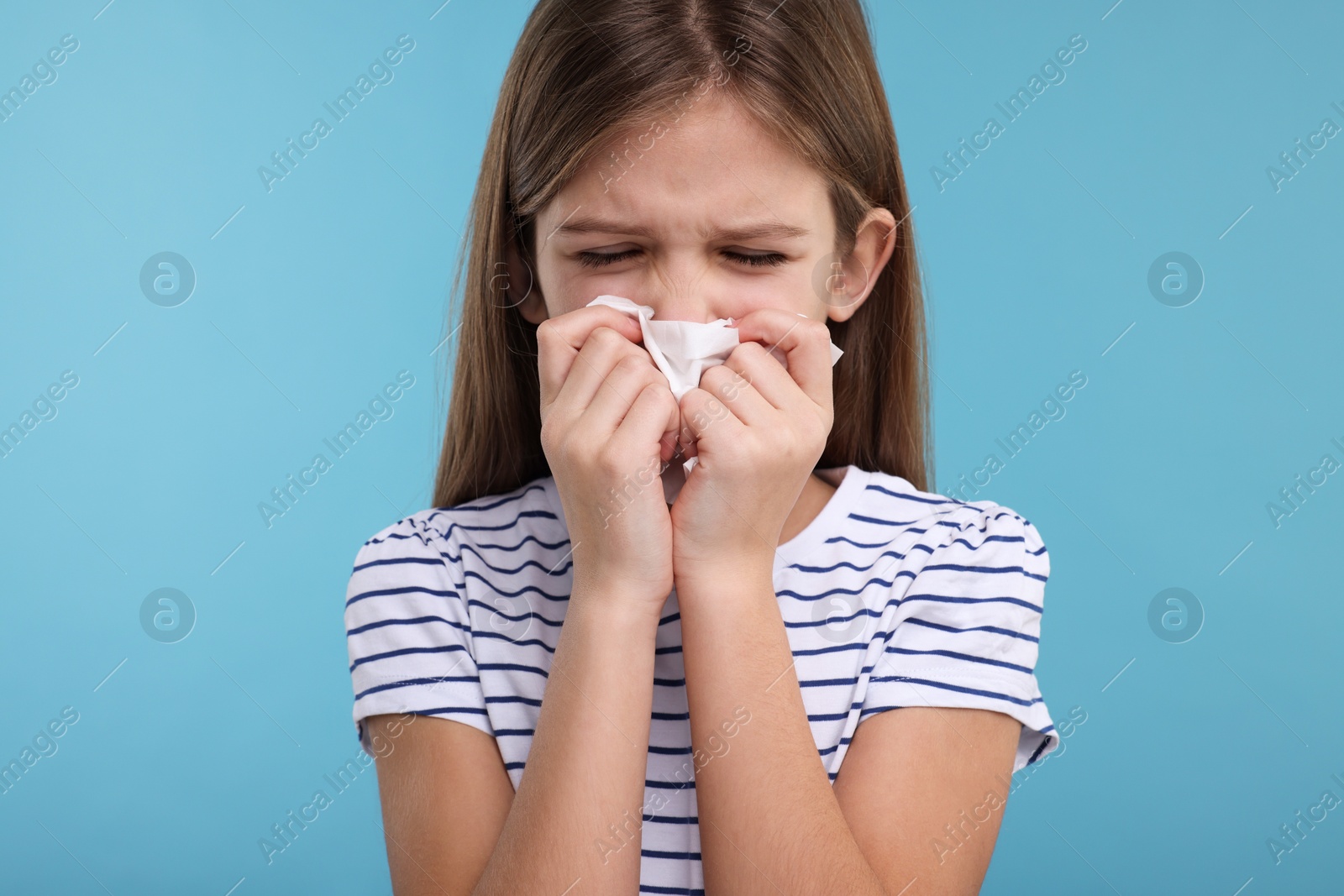 Photo of Sick girl with tissue coughing on light blue background