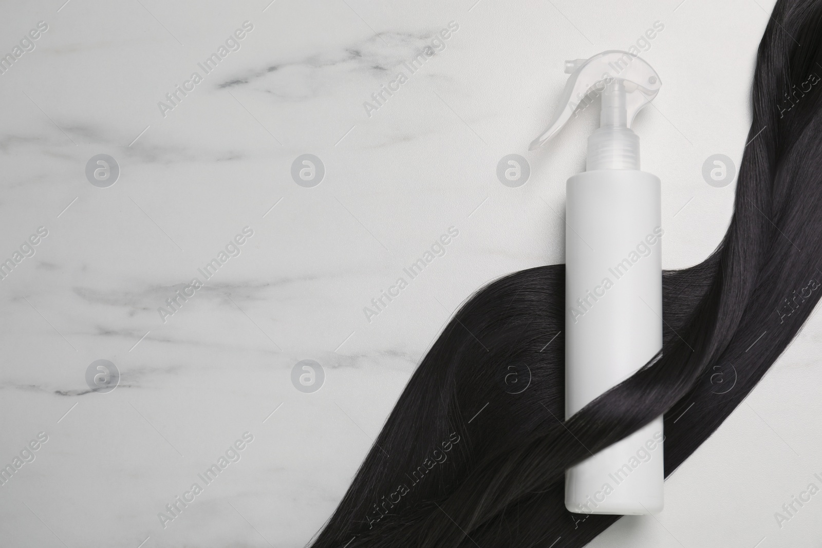 Photo of Spray bottle with thermal protection and lock of brunette hair on white marble table, flat lay. Space for text