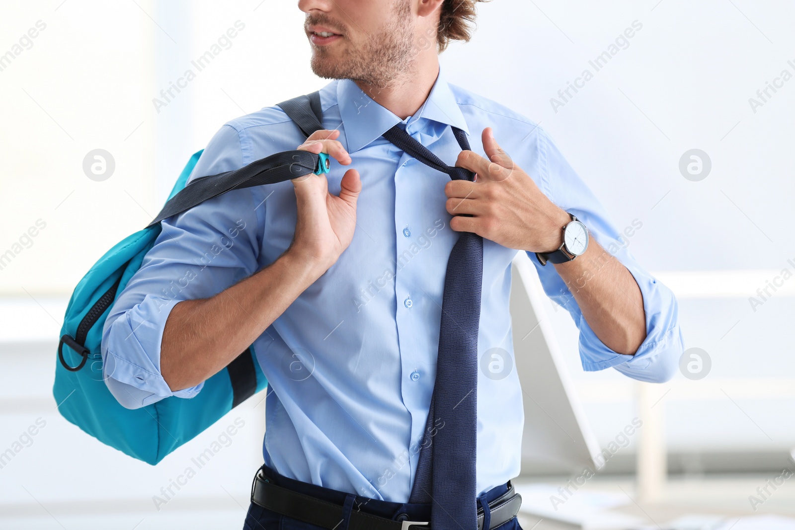 Photo of Young handsome businessman holding fitness bag in office. Gym after work