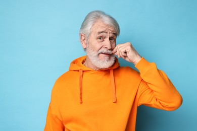 Photo of Senior man touching mustache on light blue background