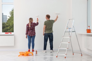 Photo of Couple painting wall in apartment during repair, back view