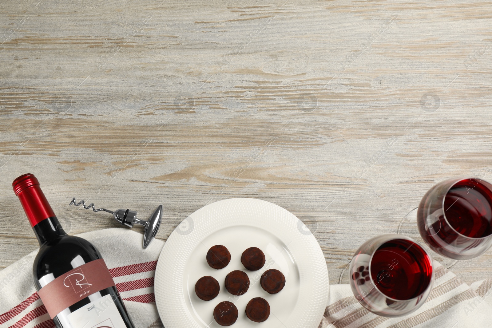 Photo of Glasses and bottle of red wine with chocolate candies on white wooden table, flat lay. Space for text