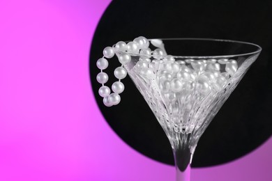 Beautiful martini glass with pearls against black circle on bright pink background, closeup. Space for text