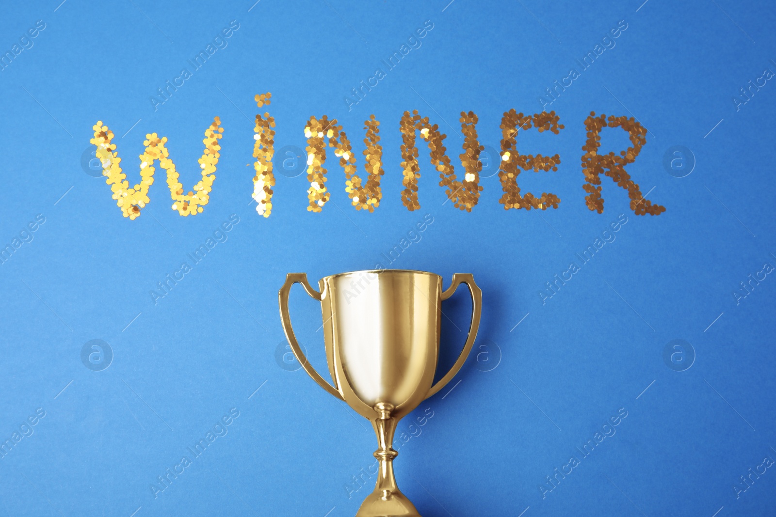 Photo of Gold trophy cup and word WINNER made with confetti on blue background, flat lay
