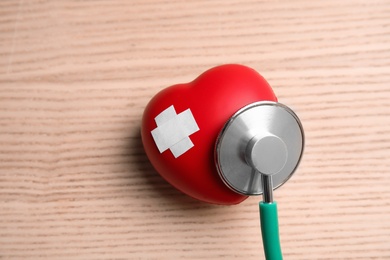 Photo of Stethoscope and red heart with adhesive plasters on wooden background, top view. Cardiology concept