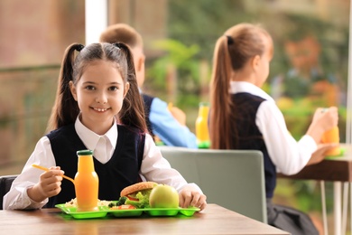 Photo of Happy girl at table with healthy food in school canteen