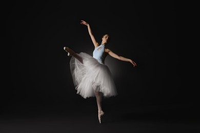Photo of Young ballerina practicing dance moves on black background