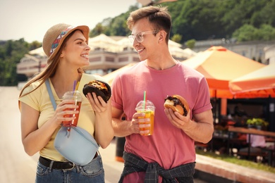 Photo of Young happy couple with burgers walking on city street