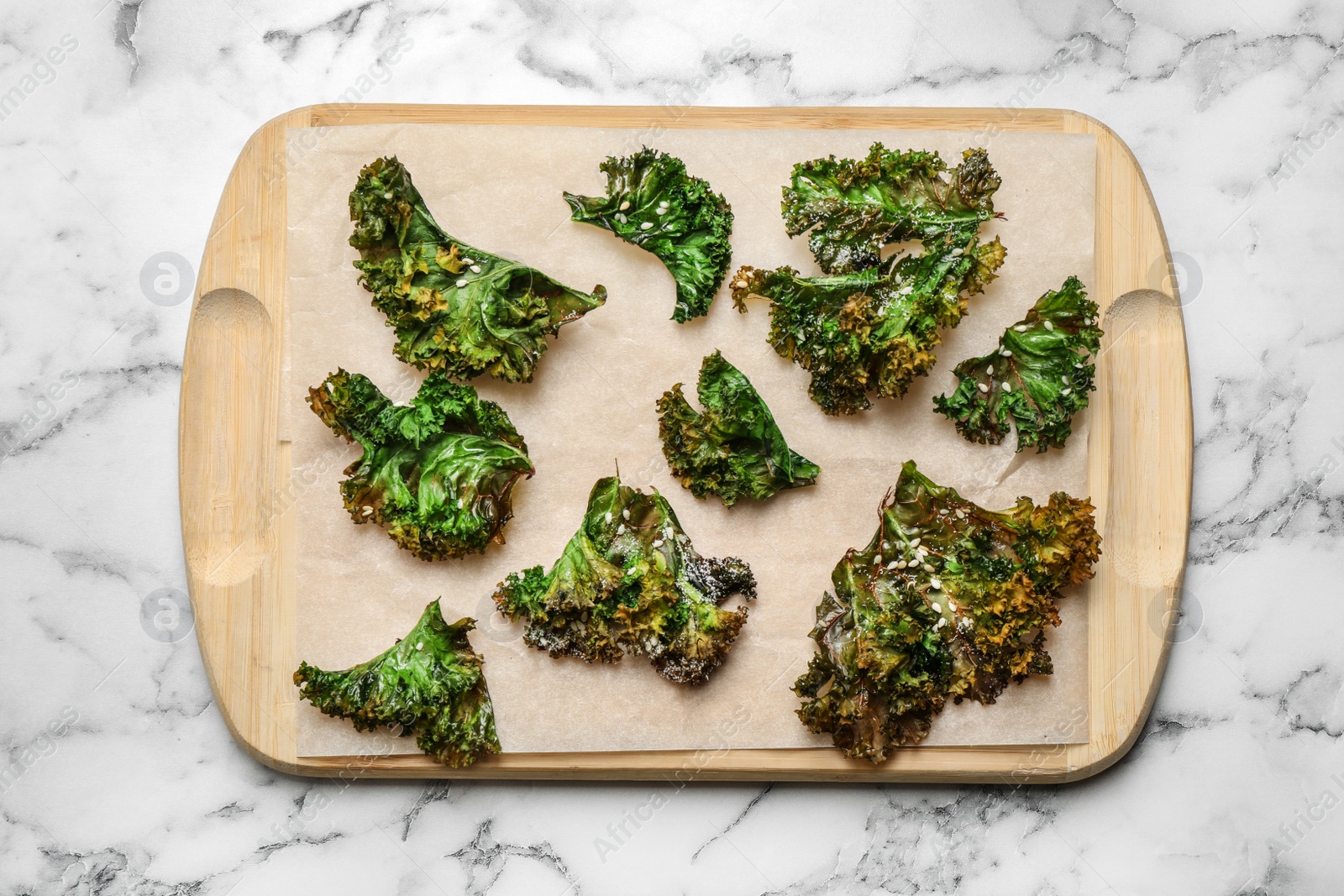 Photo of Tasty baked kale chips on marble table, top view