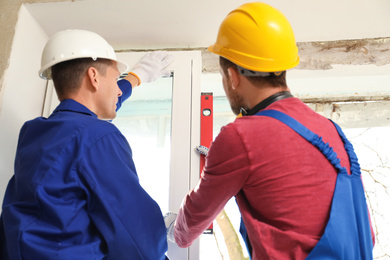 Workers using bubble level for installing window indoors