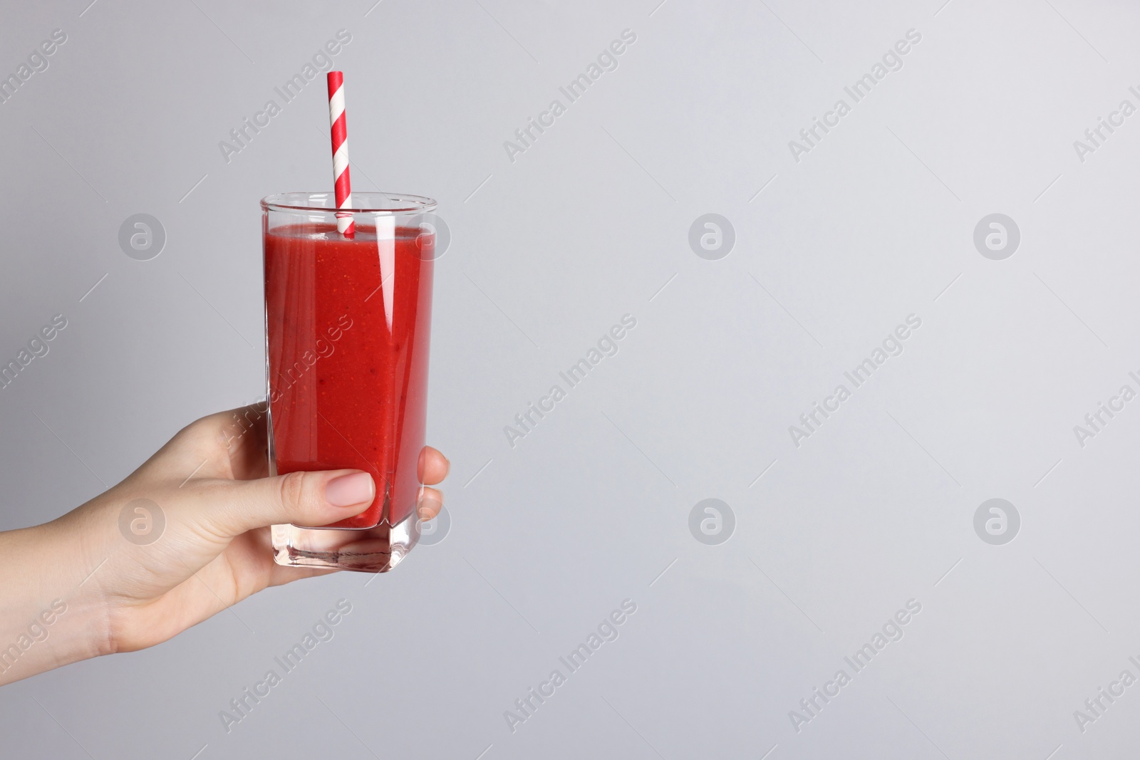 Photo of Woman holding glass of tasty smoothie on light grey background, closeup. Space for text