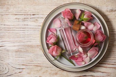 Photo of Flat lay composition with essential rose oil and flowers on white wooden table, space for text
