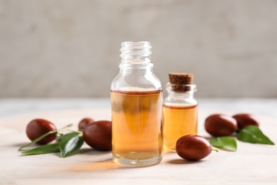 Photo of Glass bottles with jojoba oil and seeds on light table against grey background