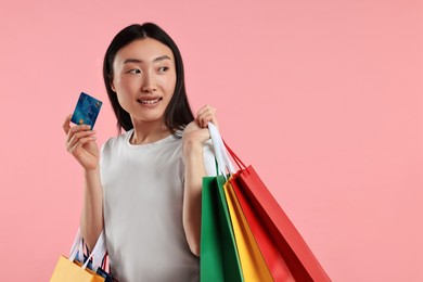 Smiling woman with shopping bags and credit card on pink background. Space for text