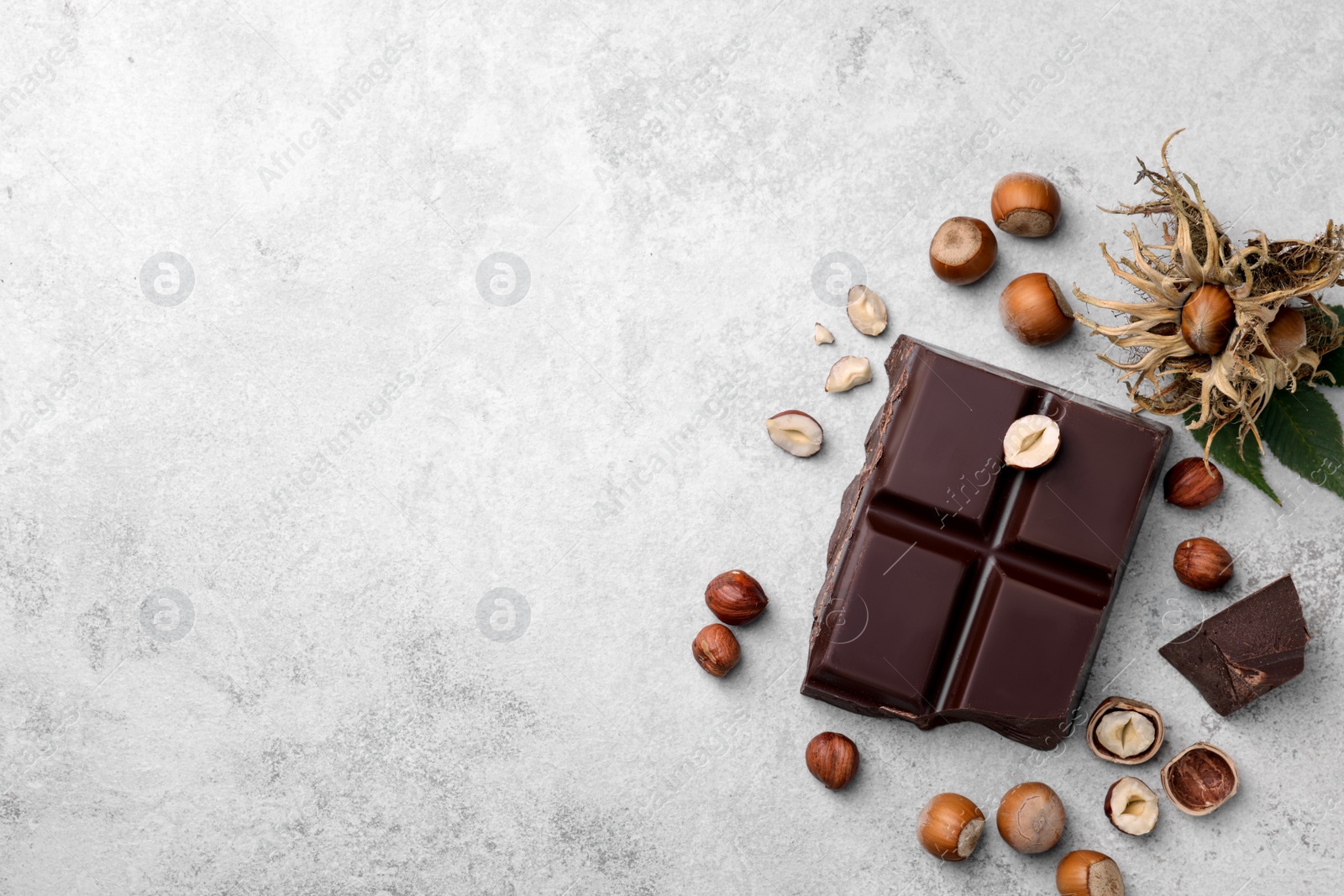 Photo of Delicious chocolate and hazelnuts on light table, flat lay. Space for text