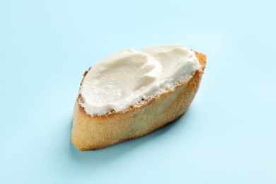 Piece of baguette with tasty cream cheese on color background