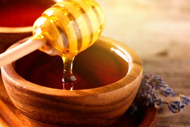 Image of Natural honey dripping from dipper into wooden bowl on table under sunlight, closeup