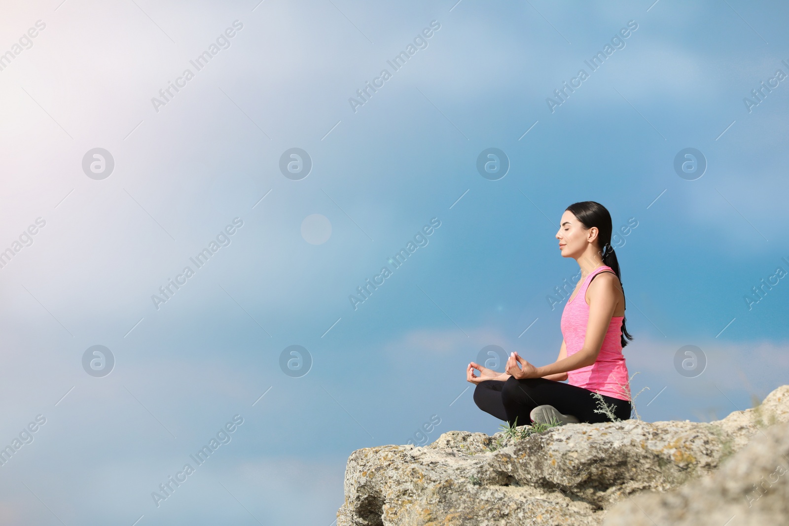 Photo of Young woman meditating on cliff. Space for text