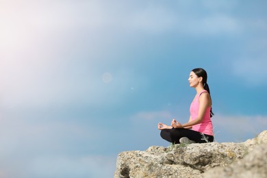 Young woman meditating on cliff. Space for text