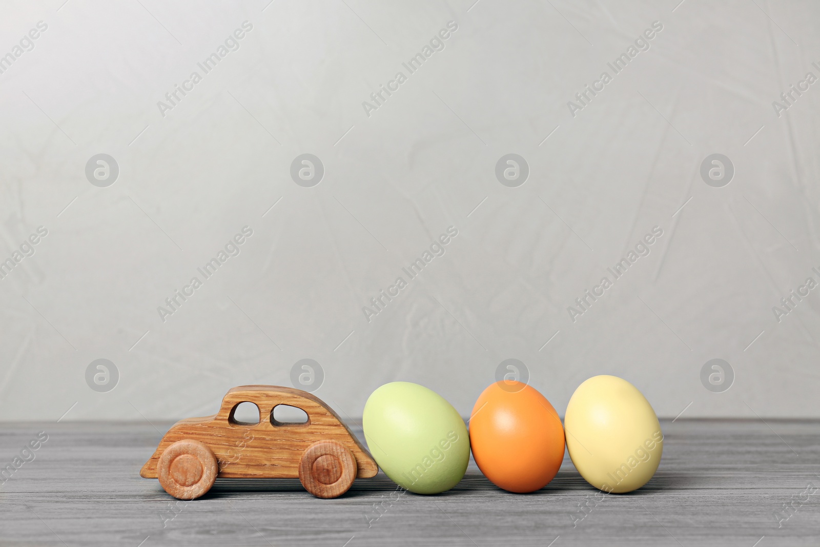 Photo of Toy car and Easter eggs on wooden table against light background