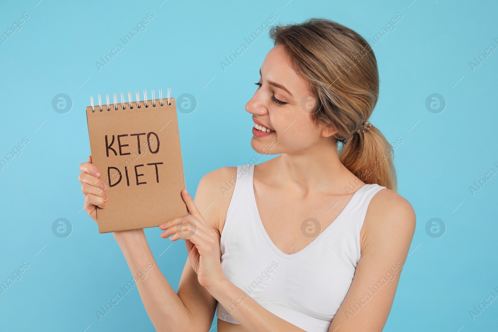 Photo of Woman holding notebook with phrase Keto Diet on light blue background