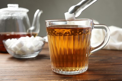 Photo of Adding sugar cube into cup of tea at wooden table, closeup