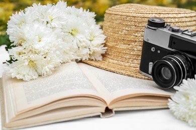 Composition with beautiful chrysanthemum flowers, vintage camera and book on white table outdoors, closeup