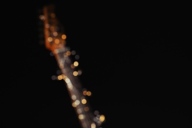 Photo of Blurred view of electric guitar with Christmas garland on black background. Space for text