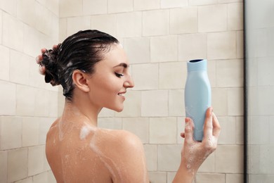 Happy woman with bottle of shampoo in shower at home. Washing hair