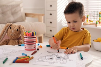 Cute child coloring drawing at table in room